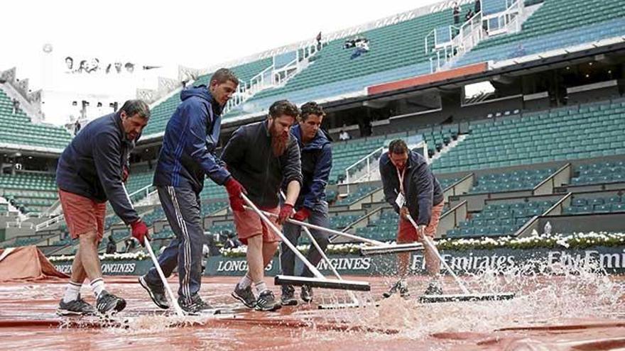 Operarios quitan agua sobre una de las encharcadas pistas de Roland Garros, ayer.