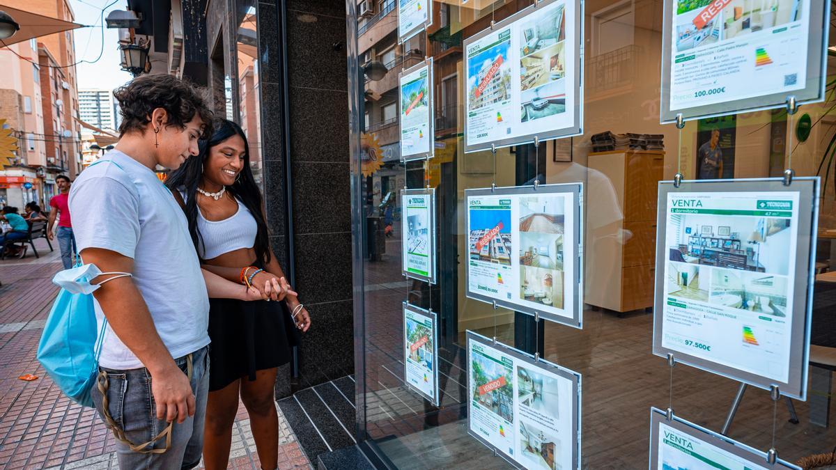 Dos jóvenes consultan ofertas de alquiler de viviendas en una inmobiliaria.