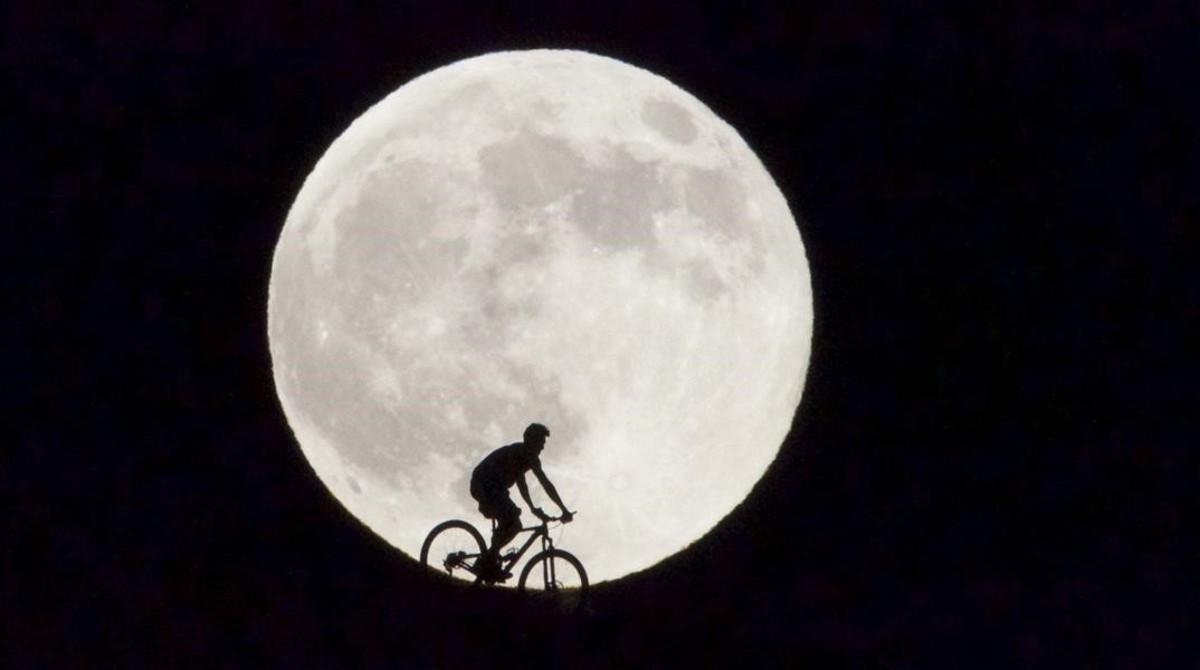 Un ciclista pasa delante de la Luna llena que en la isla canaria de Fuerteventura.