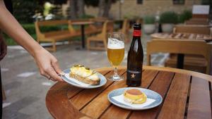 Una camarera sirve dos tapas y una cerveza en una terraza en una imagen de archivo