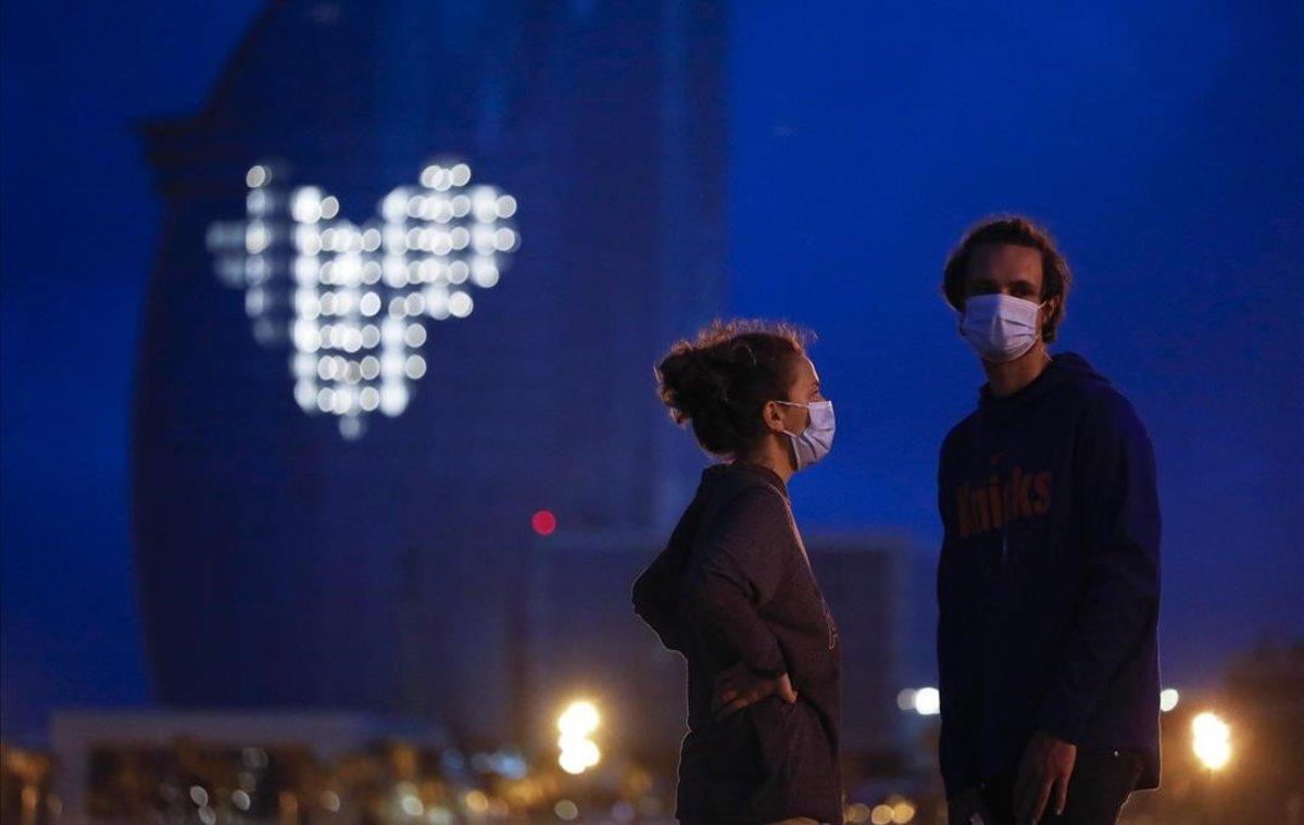 Una pareja, con el Hotel W al fondo, al anochecer, en Barcelona.