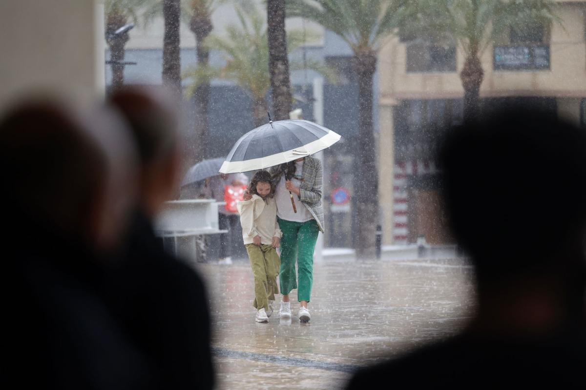 Varias personas camufladas observan a los peatones caminando bajo la lluvia en Benidorm.