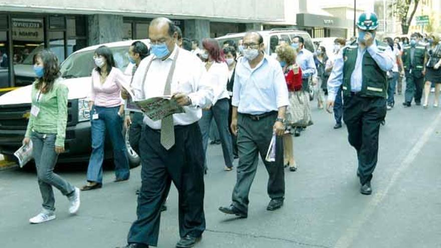 Trabajadores mexicanos, con mascarillas por la gripe porcina, desalojan un edificio tras el seísmo.