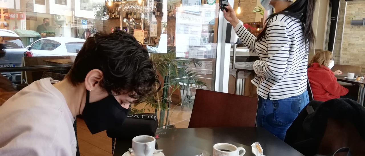 Una clienta escanea el código QR de una cafetería de Vigo, mientras otra toma un café