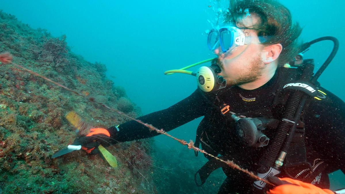 Un submarinista estirant un fil enganxat a una roca, durant l'immersió a l'Escala