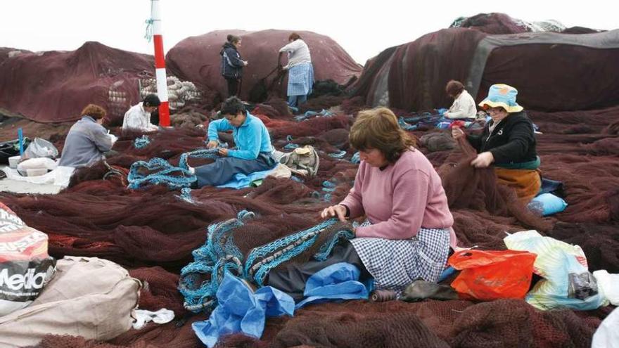 Varias mujeres reparan redes en un puerto gallego.
