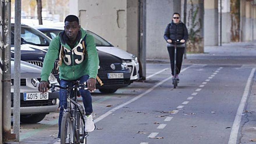 Al fons, una dona circulant amb patinet pel carril bici de Girona.