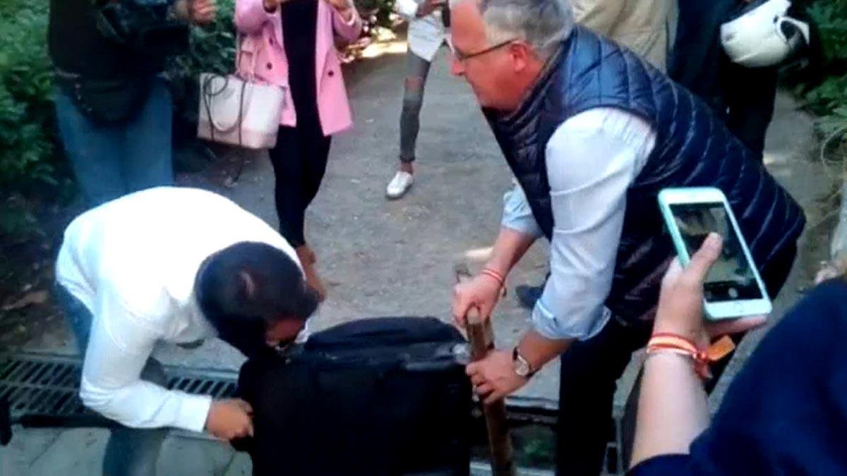 Josep Bou (PP) ayuda a una periodista a desencallar una maleta con ruedas de un desagüe