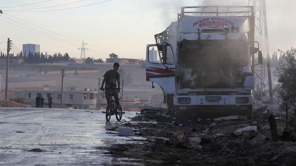 A boy rides a bicycle near a damaged aid truck after an airstrike on the rebel held Urm al-Kubra town