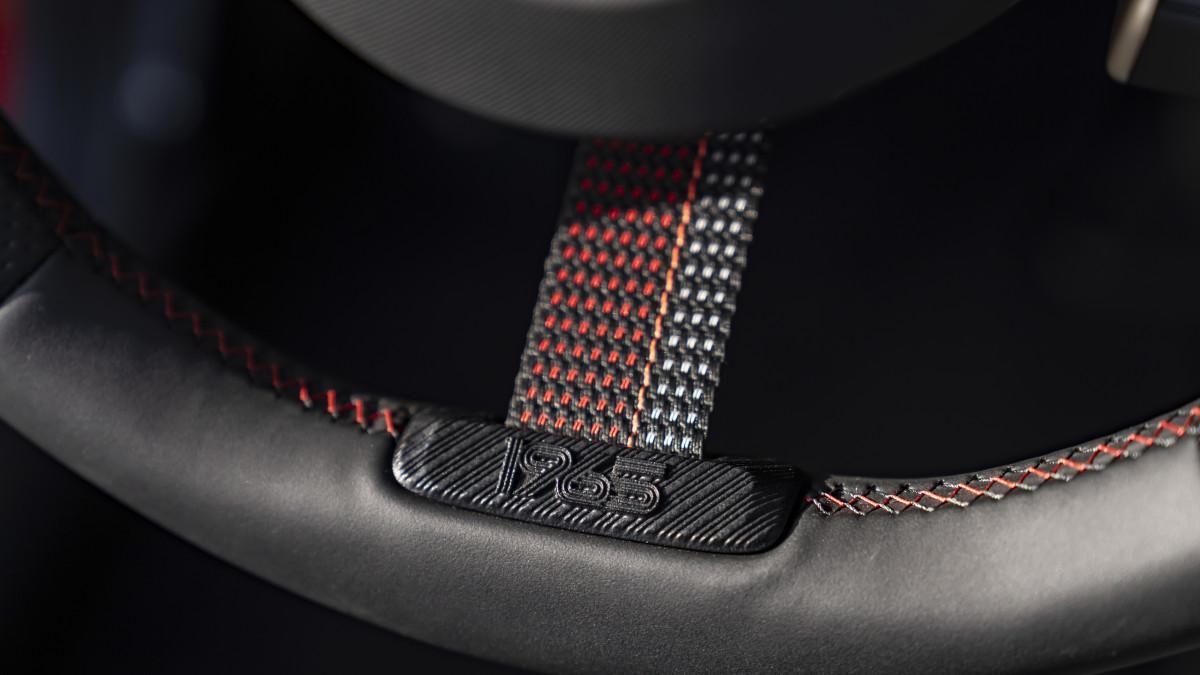 El volante deportivo incorpora el emblema “1965” en el radio inferior, integrando la herencia del rally en cada trayecto.