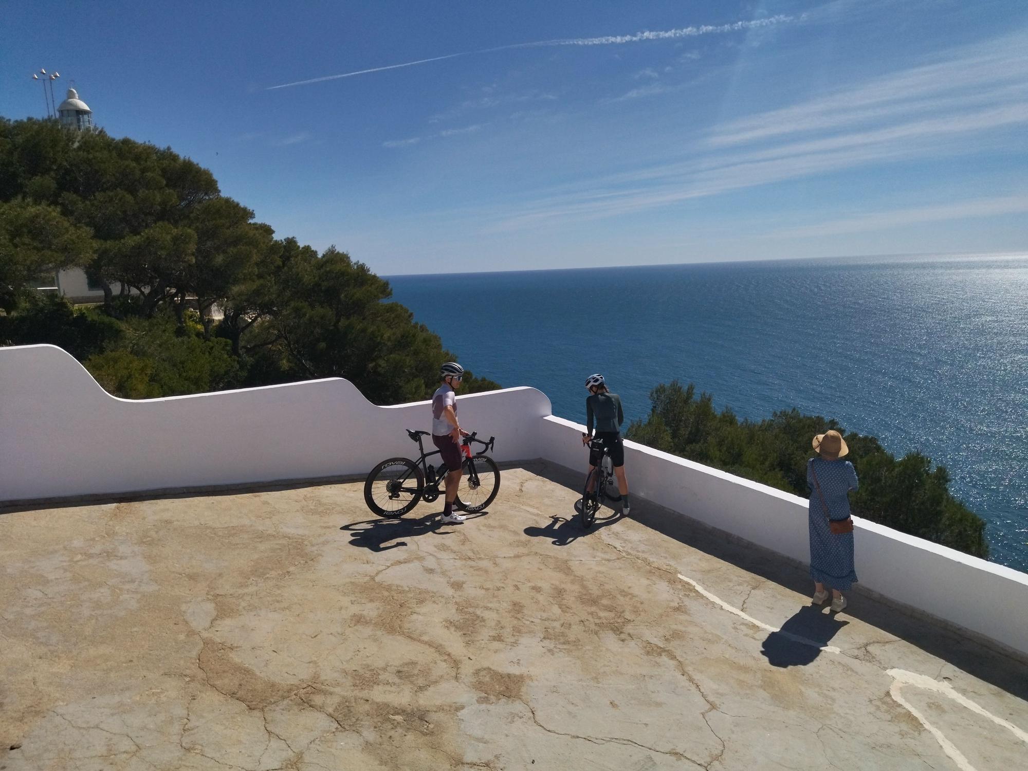 Ciclistas y una turistas otean el horizonte en el Cap de la Nau