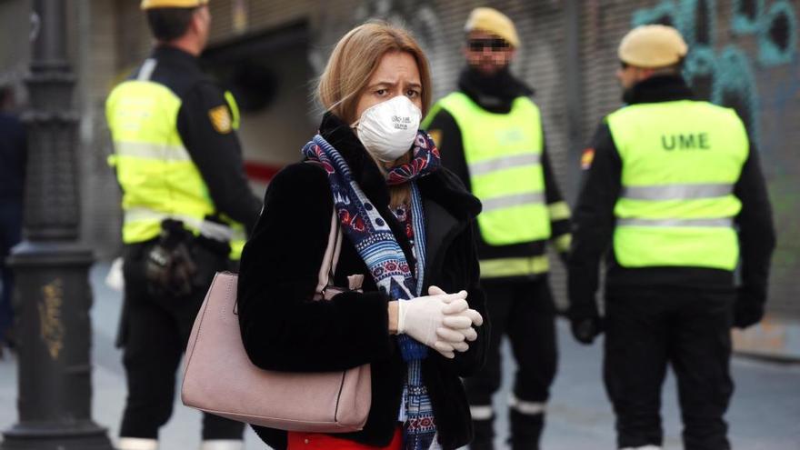 Una mujer camina protegida con una mascarilla ante un grupo de militares.