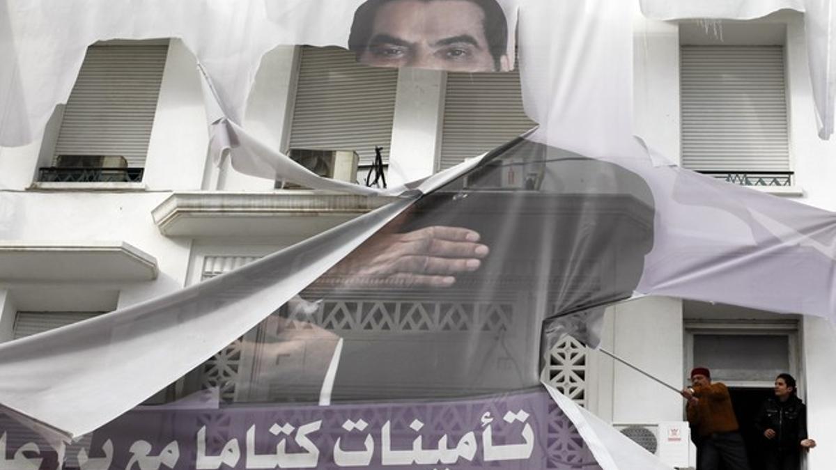 Dos tunecinos arrancan un cartel del dictador Ben Alí.