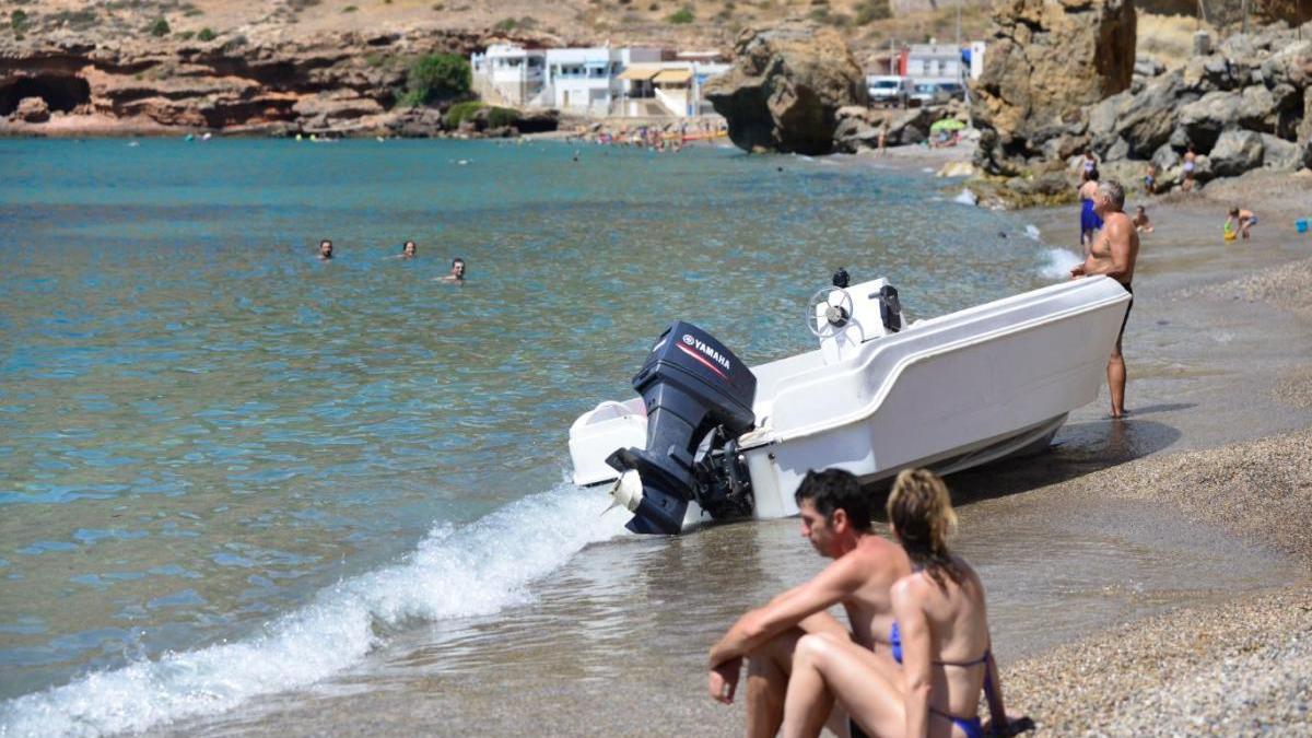 Bañistas junto a la patera abandonada en El Portús.