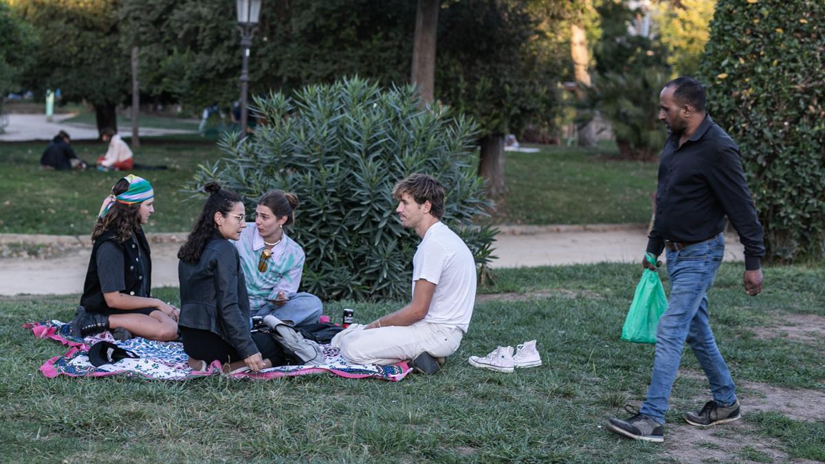 Un ’latero’ busca clientes en la Ciutadella  pasa junto a un grupo de jóvenes a los que la ordenanza prohíbe incluso tomar una lata de cerveza. 