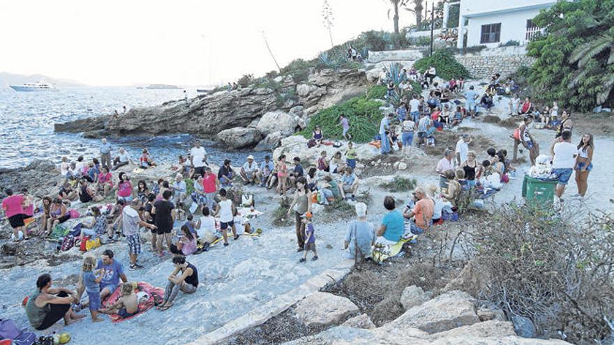 Decenas de personas sentadas en las rocas frente al mar.