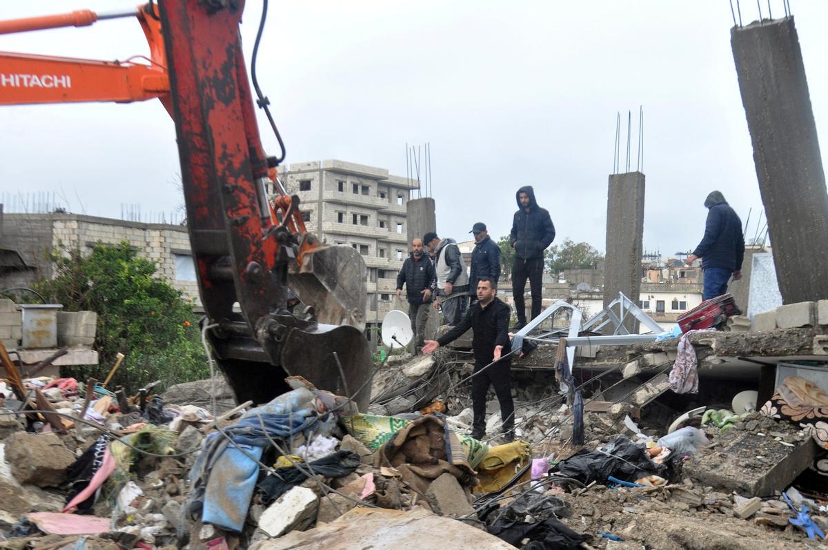 A man gestures as he stands on rubble of a collapsed building, following an earthquake, in Latakia