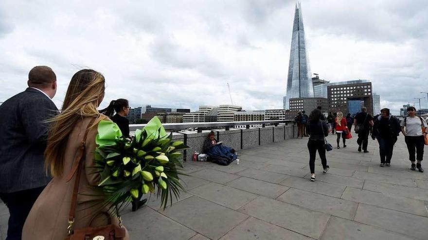 Una mujer atraviesa el Puente de Londres con un ramo de flores. A la derecha, Ignacio Echeverría. // Efe / FdV