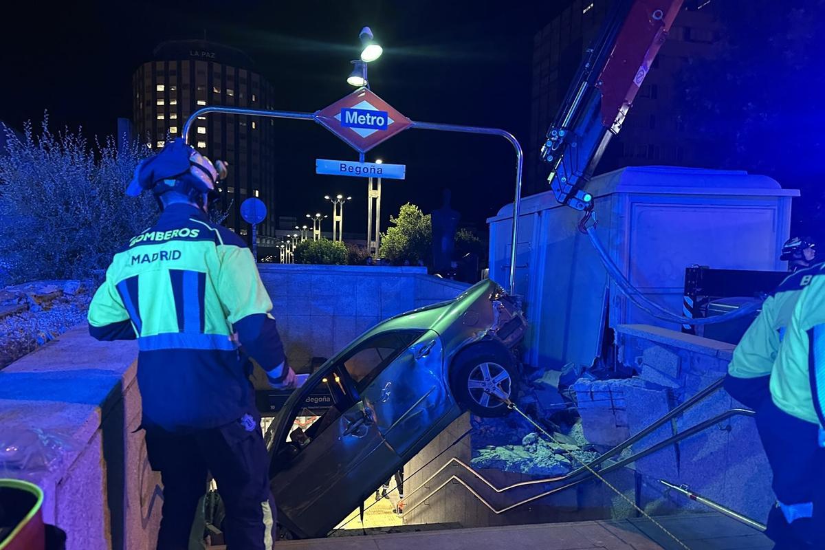 Bomberos Madrid retira mediante el uso de una grúa un vehículo encajado en las escaleras de acceso al metro de Begoña en el Paseo de la Castellana tras un accidente de tráfico