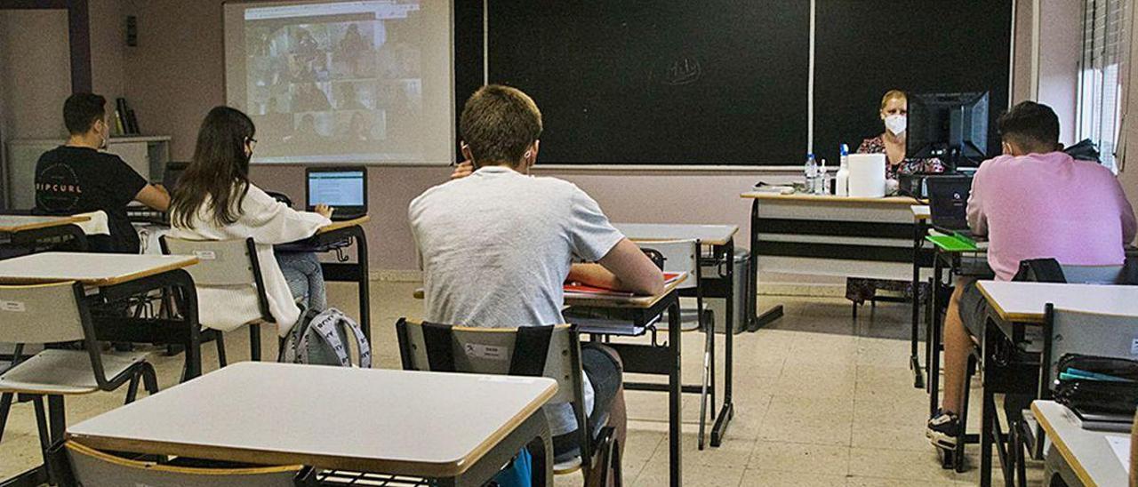 Alumnos del colegio San Fernando de Avilés, durante una clase presencial, mientras otros estudiantes (aparecen en la pantalla junto al encerado) siguen la lección en directo desde sus casas.