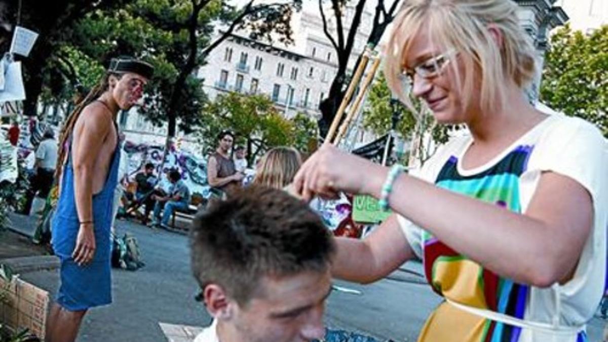 Una joven corta el pelo a uno de los acampados, ayer, en la plaza de Catalunya.
