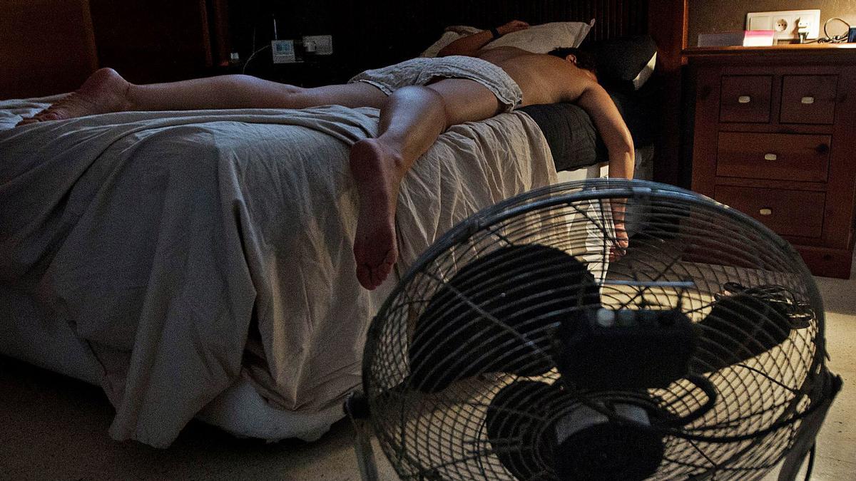 Un joven duerme echado sobre la cama junto a un ventilador para tratar de mitigar el calor nocturno. | ALEX DOMÍNGUEZ