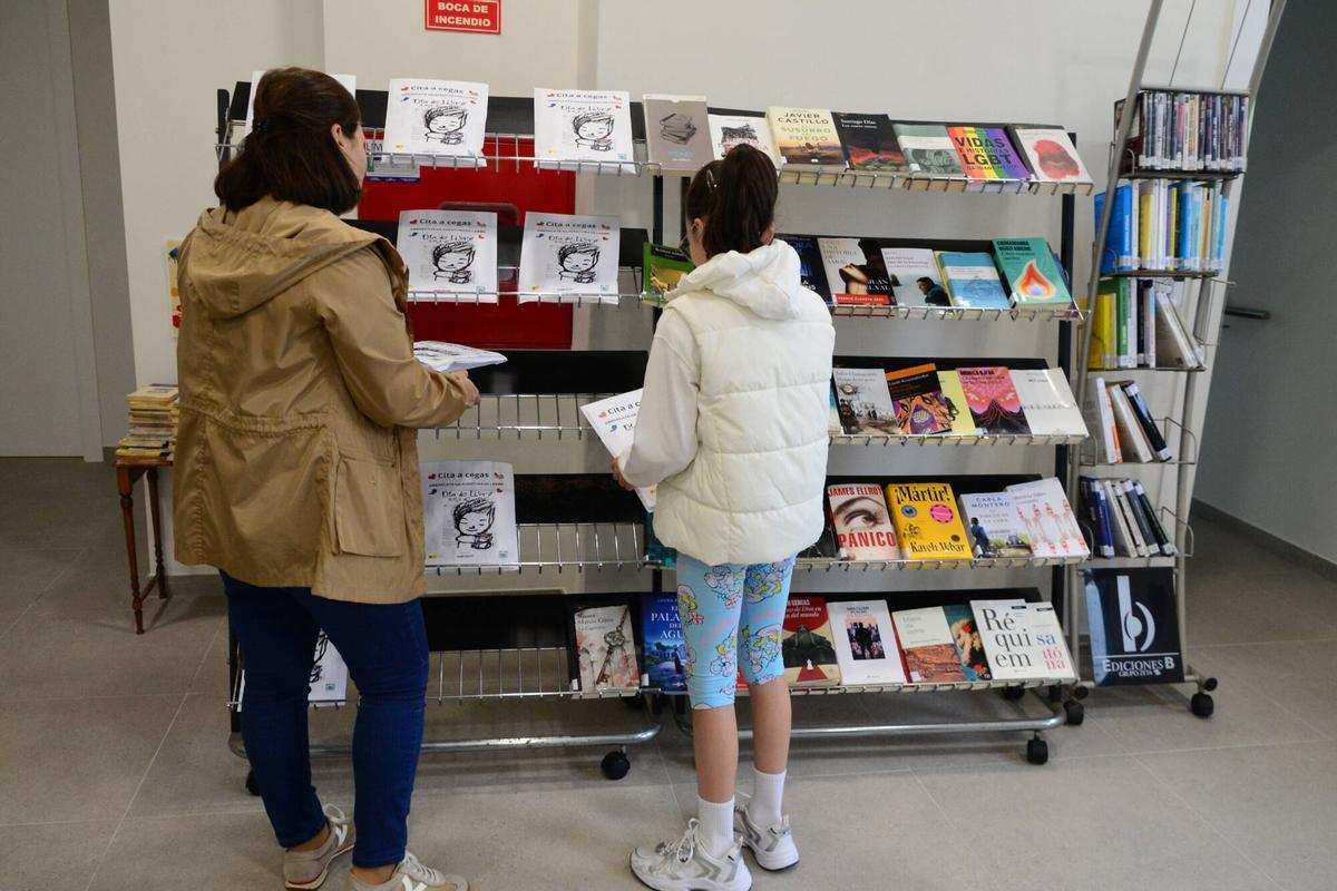 Dos lectoras, este martes, en la Biblioteca Torrente Ballester de Bueu delante del expositor donde están algunos de los libros de la iniciativa "Cita a cegas co libro"..