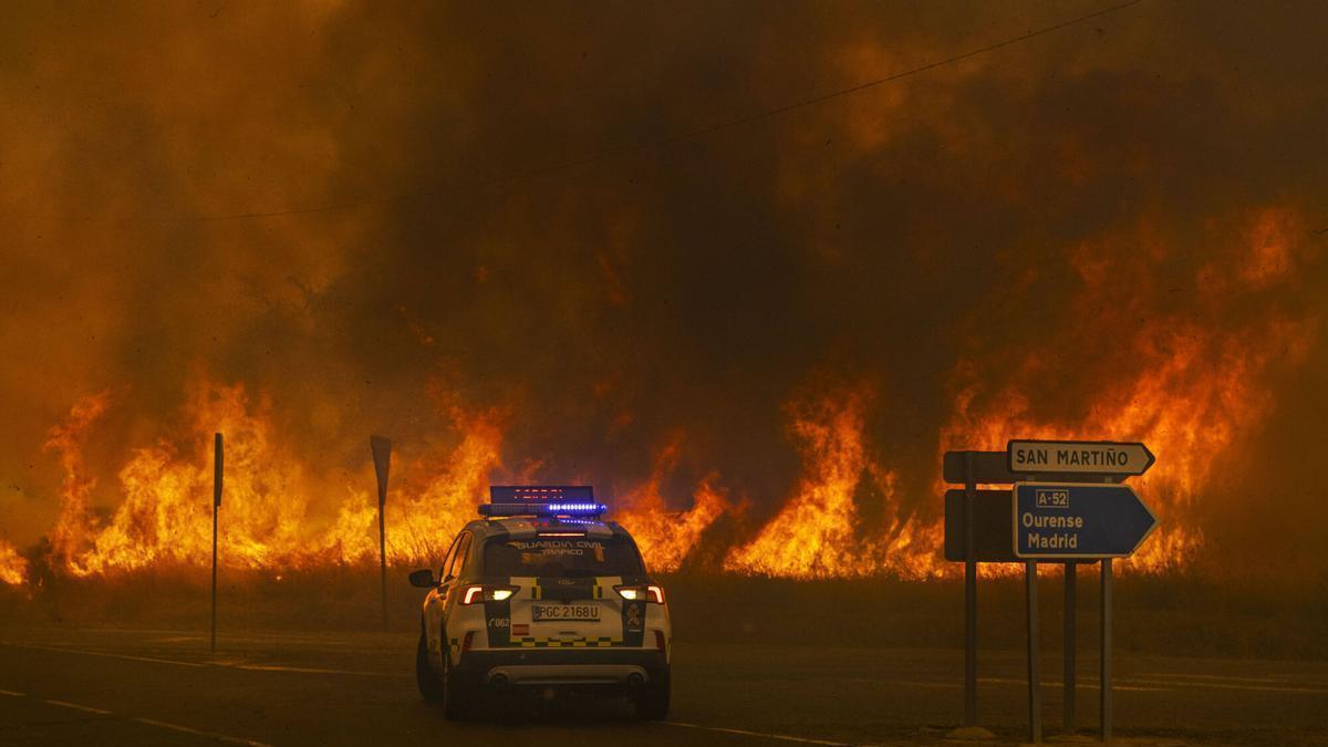 Un veículo de la Guardia Civil retrocede ante el incendio en el acceso a la autovía Ourense_Madrid, en Cualedro en agosto de 2025. ENDIOS FORESTALES, SE PRODUJERON NUMEROSOS CORTES EN LAS COMUNICACIONES, EL 15 DE AGOSTO DE 2025. LLAMAS. NOCHE. COCHE PATRULLA