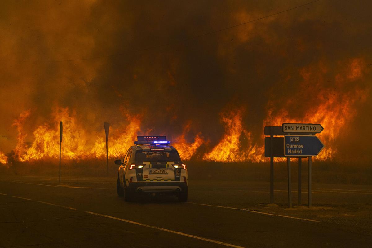 Un coche de la Guardia Civil retrocede ante el incendio en el acceso a la autovía A-52 en Cualedro.