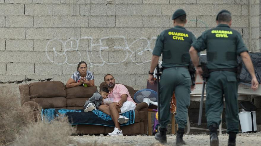 Dos guardias civiles se dirigen a tres personas sentadas en un sofá en el desalojo.