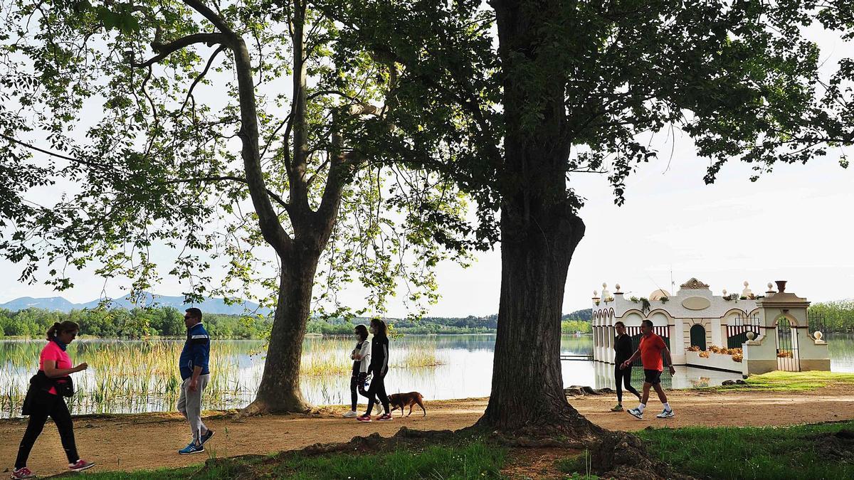 Gent passejant i caminant per un tram del passeig de l’estany on es pot veure una de les tradicionals i ben conservades pesqueres. | PERE DURAN