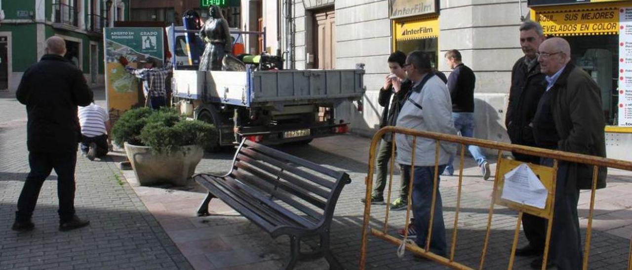 Los vecinos observan las obras, con la estatua al fondo, cargada en el camión municipal.