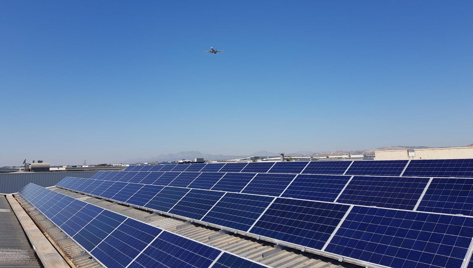 Un avión sobrevolando los tejados con paneles solares de las naves industriales del Parque Empresarial de Elche.