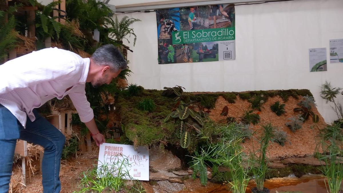 El concejal Javier Caraballero coloca el cartel del primer premio de Jardinería en la carpa del IES El Sobradillo.