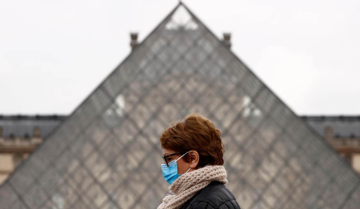 Una mujer con mascarilla pasa frente a la pirámide del Louvre, en París