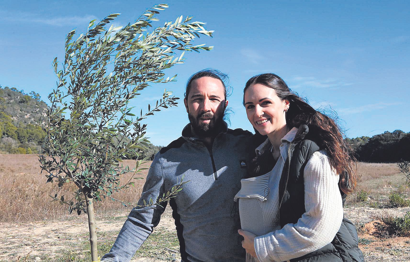 In einer Hand hält Benjamin Kern einen jungen Olivenbaum, den Arm legt er um seine Frau Carina, Baby Nola steckt im Tragetuch.