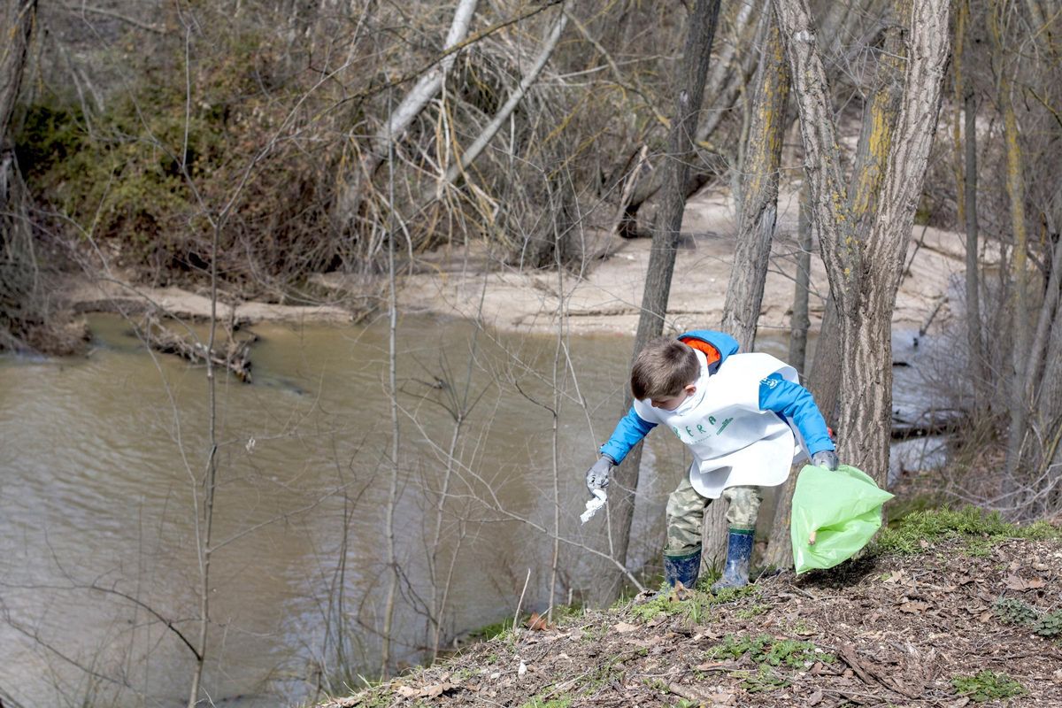 Un niño recoge basuraleza junto a un río.