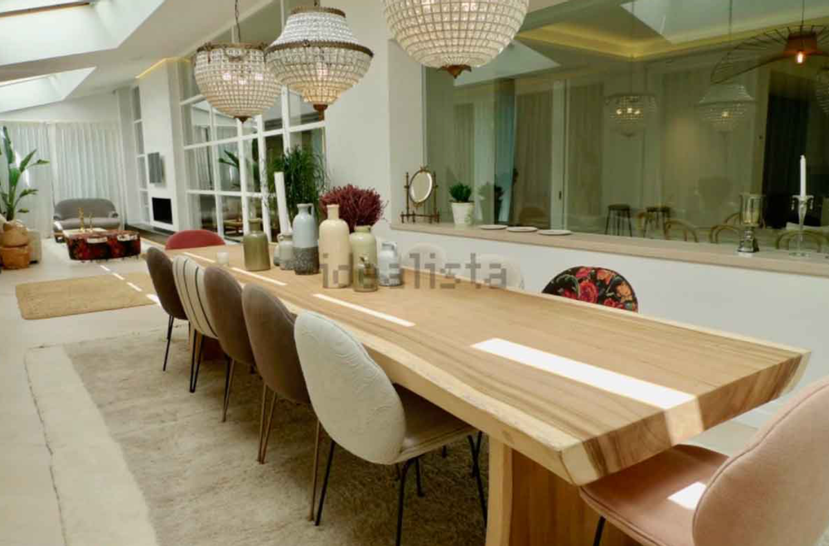 Será por mesas en esta casa, por sillas o por espacio para invitados. Este es el comedor principal de la mansión con mesa de acabado efecto tronco natural de madera. Sillas acolchadas de distintos colores y tres lámparas de cristal. Todo junto a la cocina y una de las salitas, la que tiene solarium.