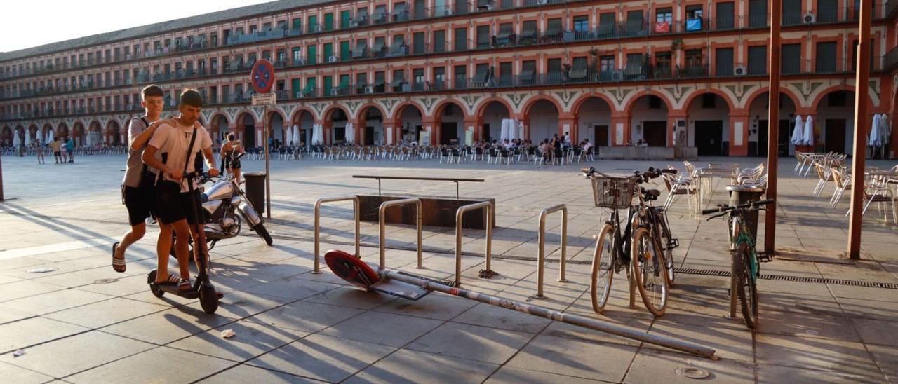 Unos jóvenes circulan con un patinete, junto a una señal caída, en la plaza de la Corredera de Córdoba.