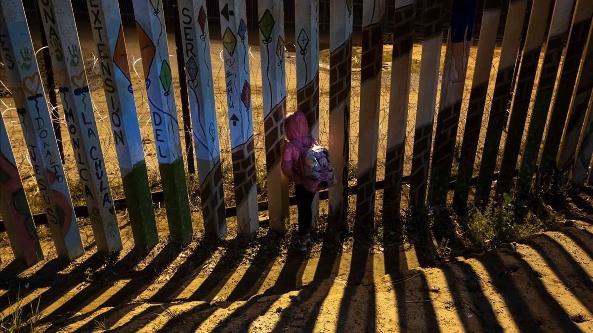 Britany, una niña hondureña de siete, años mira a través de la valla fronteriza en Tijuana hacia EEUU.