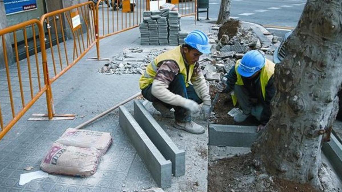 Unos obreros realizan obras en una acera de las calles de Barcelona