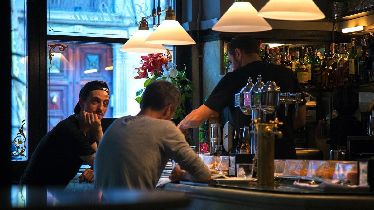 Personas en la barra de un bar, comiendo tapas para acompañar la bebida