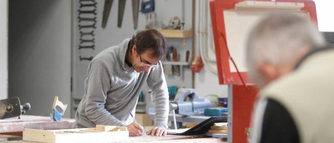 Arriba, dos hombres trabajan en el taller de carpintería del centro de formación de La Corredoria. Al lado, Rosón se dirige a los participantes en el programa; a la izquierda de la foto, Marcos Cienfuegos.