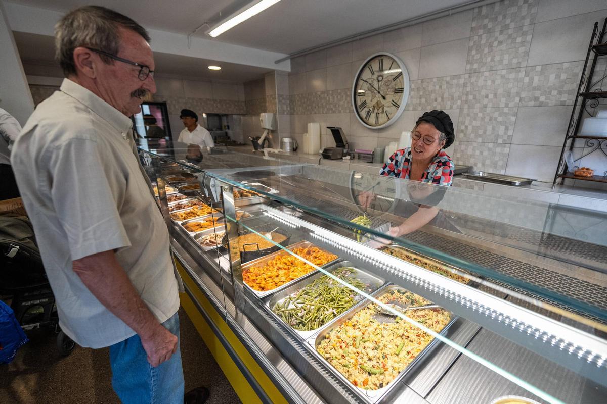 Núria, dependienta de la tienda Cuina Cassola, sirve un plato de comida preparada a un cliente.