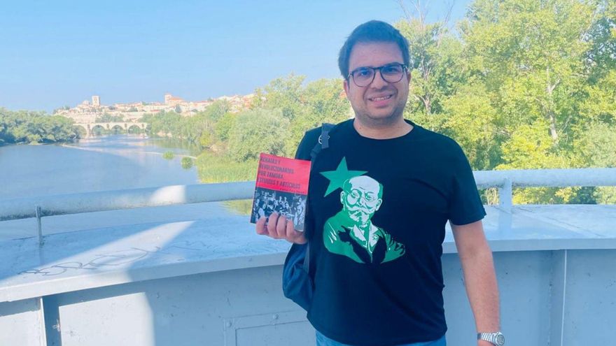 El investigador Carlos Coca con su nuevo libro en el Puente de Hierro con la Catedral, de fondo. | Cedida