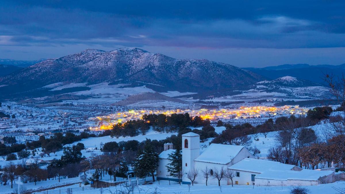 Vista invernal de María, en la comarca de Los Vélez (Almería), con el casco urbano iluminado y la Sierra de María-Los Vélez cubierta de nieve al fondo