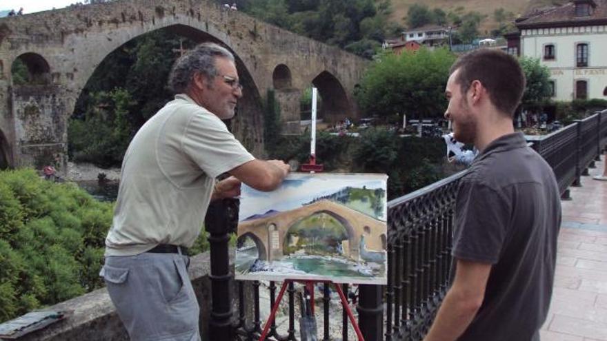 Pepe Sumariva ante el «puente romano» de Cangas de Onís, con uno de sus cuadros. / carbajal