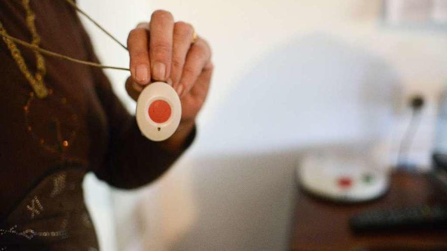 Una mujer muestra el colgante con el botón de alerta de la teleasistencia básica.