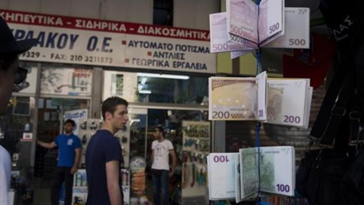 Ciudadanos griegos pasean ante carteras con el diseño del euro en un quiosco del centro de Atenas, este martes.