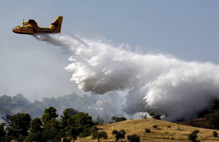 A firefighting plane drops water over holiday homes in southeastern Greece